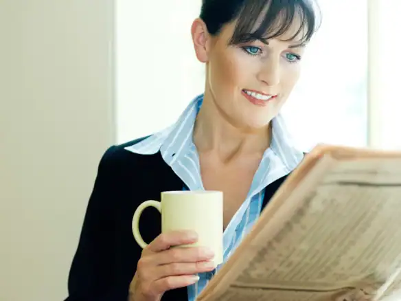 Professional woman enjoying coffee and reading newspaper at workplace.