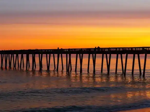 Beautiful sunset view over Pensacola Beach pier reflecting on water.